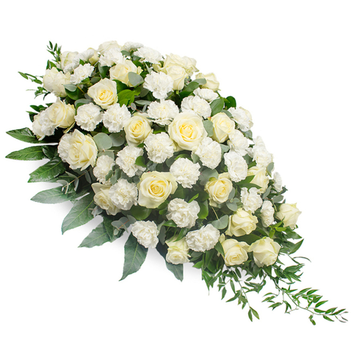 A luxurious funeral spray composed of white and cream blooms lies gracefully on a white background, its design forming a classic elongated teardrop that is fullest at the upper left and gradually narrows to a slender point at the lower right. At the centre of this arrangement, numerous white and soft ivory roses are closely packed, some still in bud and others fully open, their layered, spiralling petals creating a rich, velvety surface that draws the eye. Between these larger focal flowers, delicate white carnations are tucked in, their ruffled petals providing texture and a gentle, billowing softness that contrasts with the smooth rose petals. Supporting the entire spray is a generous base of foliage: deep-green leaves provide structure, while muted, bluish-green eucalyptus and fine, trailing ruscus stems wind among the blooms and extend beyond the edges, particularly along the tapering right side. These trailing greens emphasise the sense of movement and give the arrangement a flowing, almost river-like line, reminiscent of the peaceful paths and open skies around Kingston Vale and nearby Richmond Park. The lighting is bright and even, accentuating the purity of the white flowers and the subtle shades of green while casting soft shadows that reveal the dimensional craftsmanship. This is the type of dignified tribute a family might choose for a funeral or memorial service, whether in a local church close to Kingston Vale or at a nearby crematorium. The white and green colour palette symbolises innocence, serenity, and lasting respect, offering a quiet focal point of comfort for mourners and a graceful floral expression of farewell for the person being honoured.